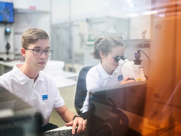 Zwei junge Menschen am Arbeitsplatz mit Mikroskop und Monitor