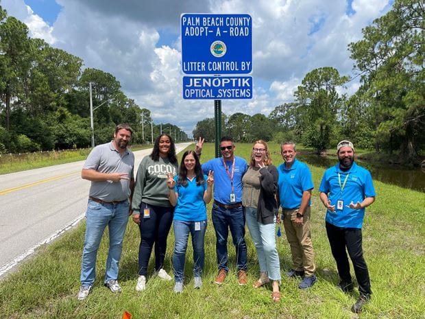 Jenoptik-Mitarbeter vor einem blauen Schild der Aktion "Adopt a Road" in Florida